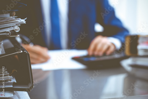 Binders with papers waiting to be processed with businessman or bookkeeper back in blur. Accounting planning budget. Audit, insurance and business concept