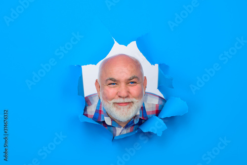 Smiling bearded man through hole in blue paper. Discount. Sale. Season sales. Sellout. Through paper. Advertising. Emotions. Discount, sale, season sale. Happy man through paper.