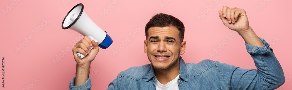 Panoramic shot of disappointed man with loudspeaker looking at camera isolated on pink
