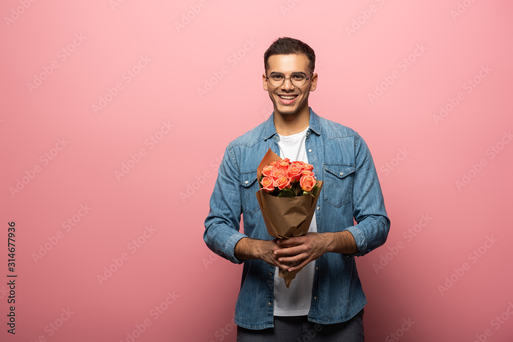 Handsome man smiling at camera while holding bouquet on pink background - obrazy, fototapety, plakaty 