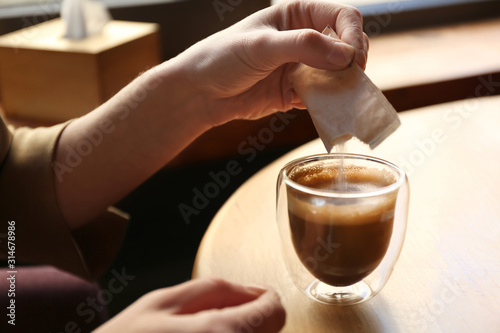 Woman adding sugar to aromatic coffee at table in cafe, closeup