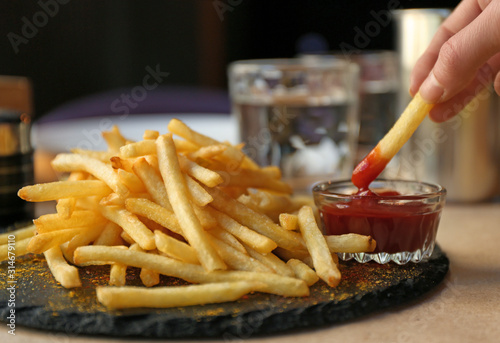 Fotografia Woman dipping French fries into red sauce in cafe, closeup