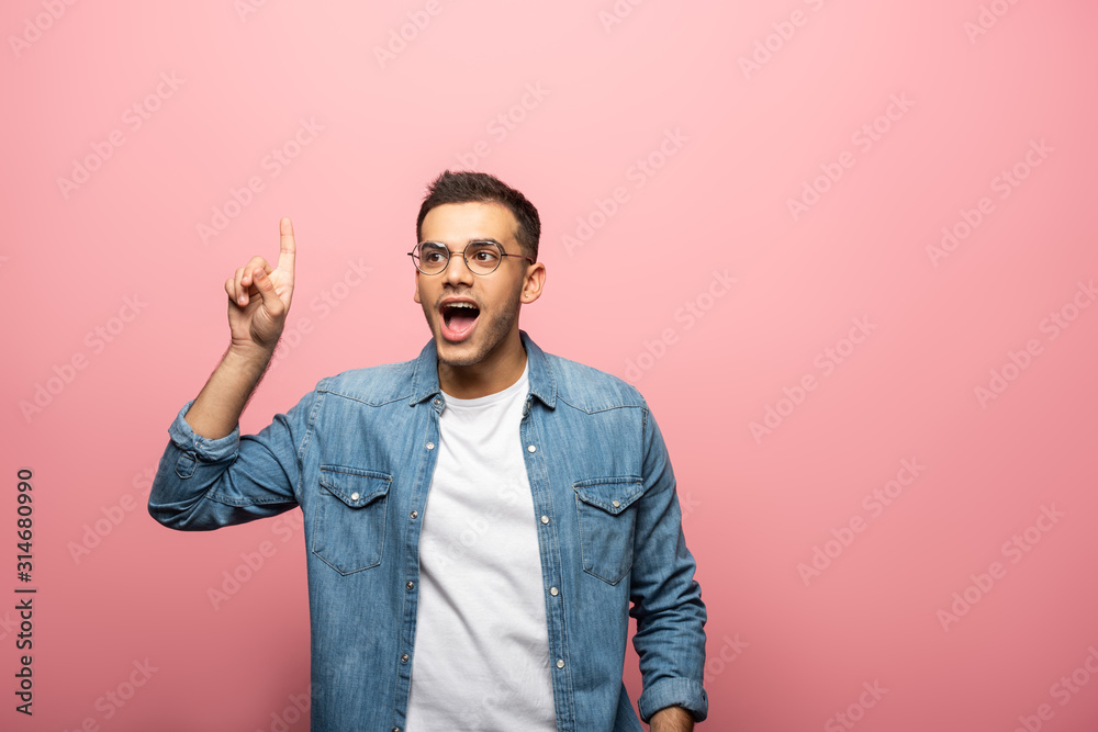 Excited young man pointing with finger on pink background Excited young man pointing with finger on pink background