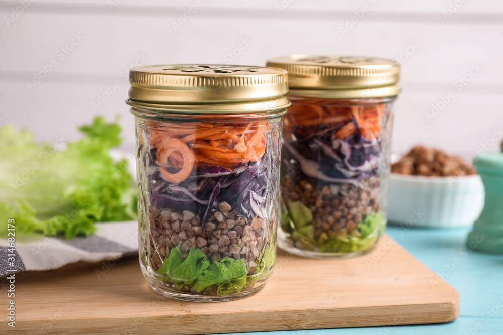 Glass jars with healthy meal on light blue wooden table Glass jars with healthy meal on light blue wooden table