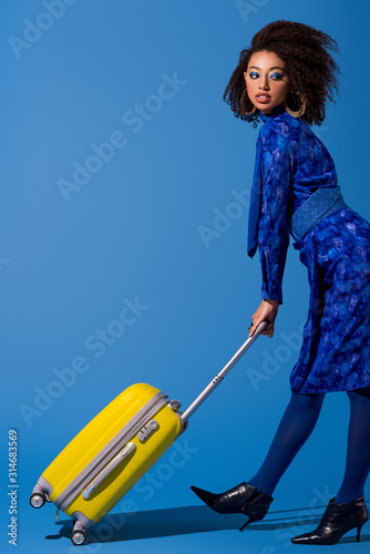 african american woman holding travel bag on blue background