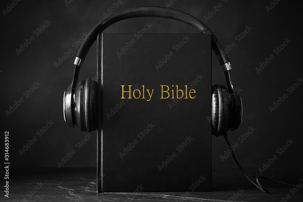 Bible and headphones on black background. Religious audiobook - obrazy, fototapety, plakaty 