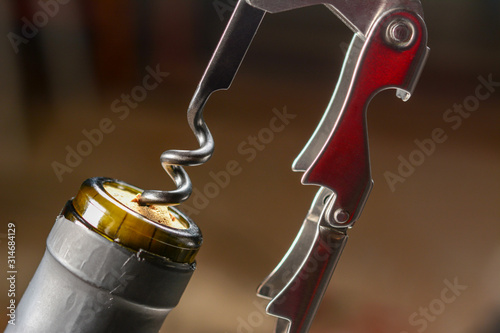 Professional sommelier or waiter knife, pulls out a cork from the bottle of red wine. Corkscrew and bottle opener close-up macro in dark key.
