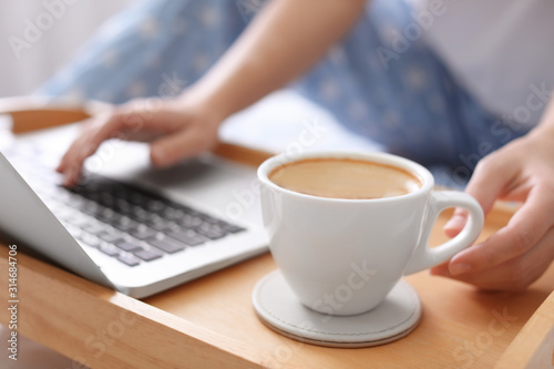 Woman taking cup of morning coffee while working on laptop indoors, closeup