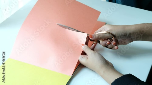 Woman hands using scissors for cutting orange paper card for craft