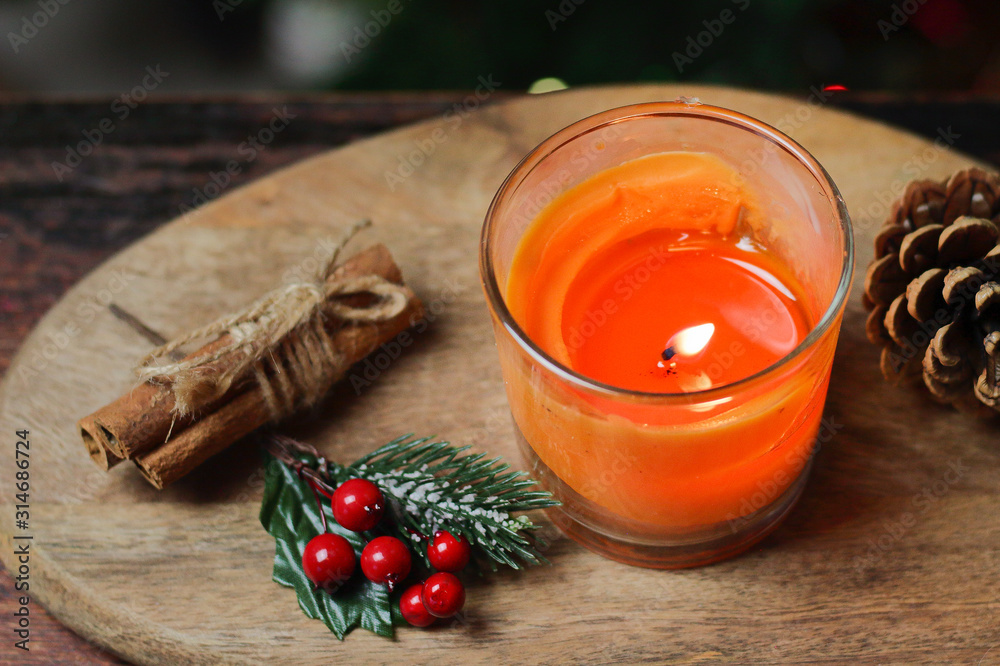 Beautiful Christmas orange mandarin candle on a wooden stand with sticks of whole cinnamon, sprig of mistletoe and a Christmas tree decorated with toys. Christmas New year evening mood, greeting card Beautiful Christmas orange mandarin candle on a wooden stand with sticks of whole cinnamon, sprig of mistletoe and a Christmas tree decorated with toys. Christmas New year evening mood, greeting card