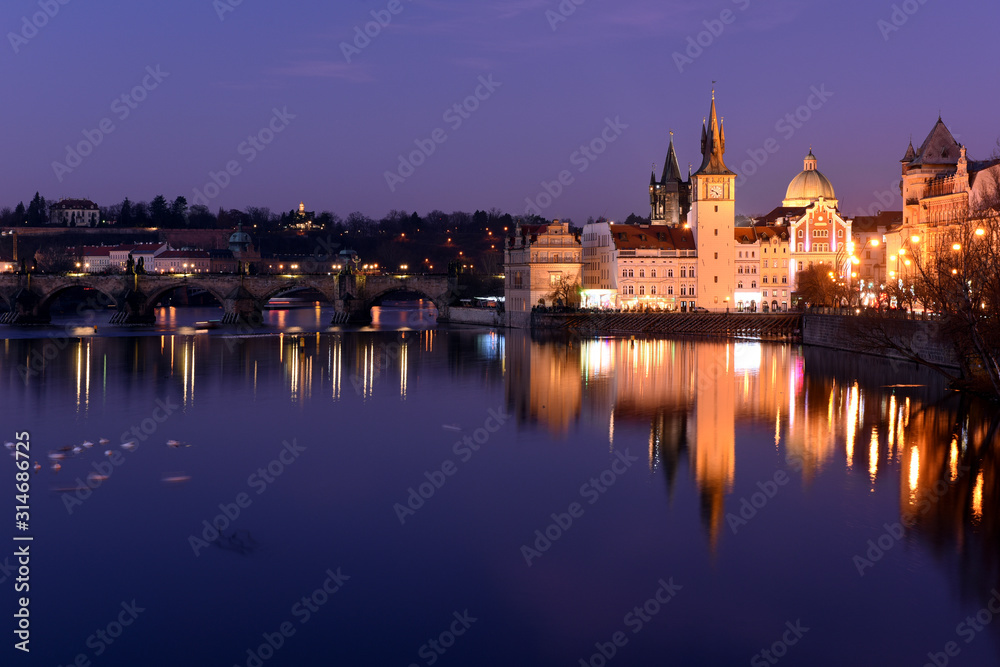 Urban scene with old Town Bridge Tower, clock tower and St. Francis Of Assisi Church in Prague, Czech Republic while sunset