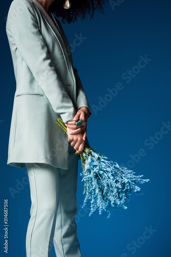 cropped view of african american woman holding bouquet isolated on blue