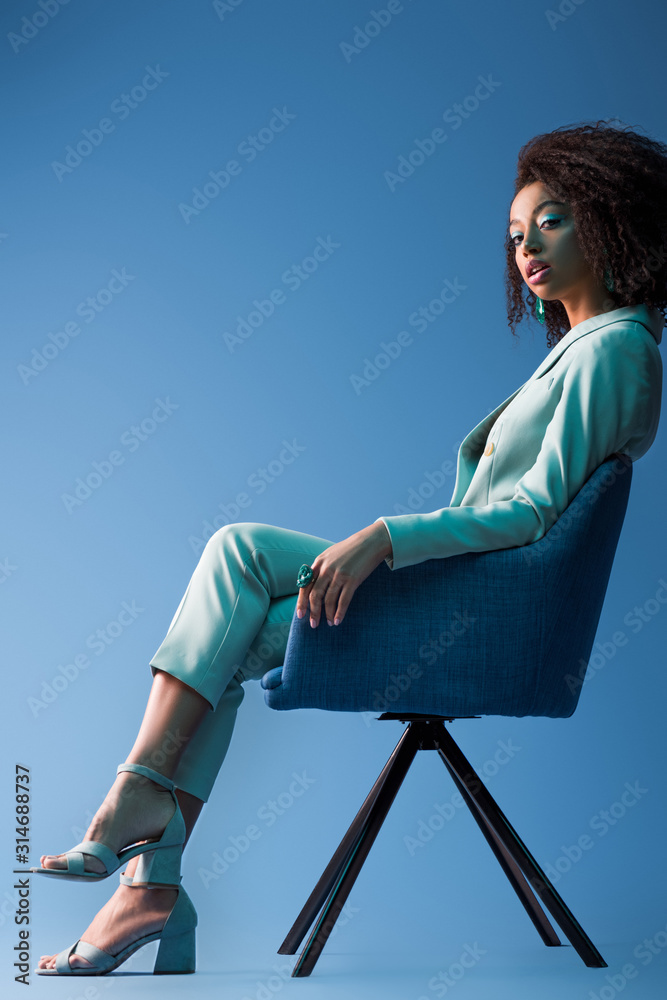 african american woman sitting on armchair on blue background