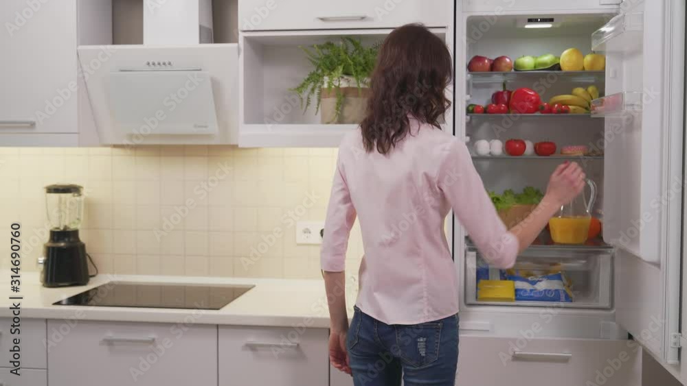 Young mom taking orange juice from refrigerator for daughter Young mom taking orange juice from refrigerator for daughter