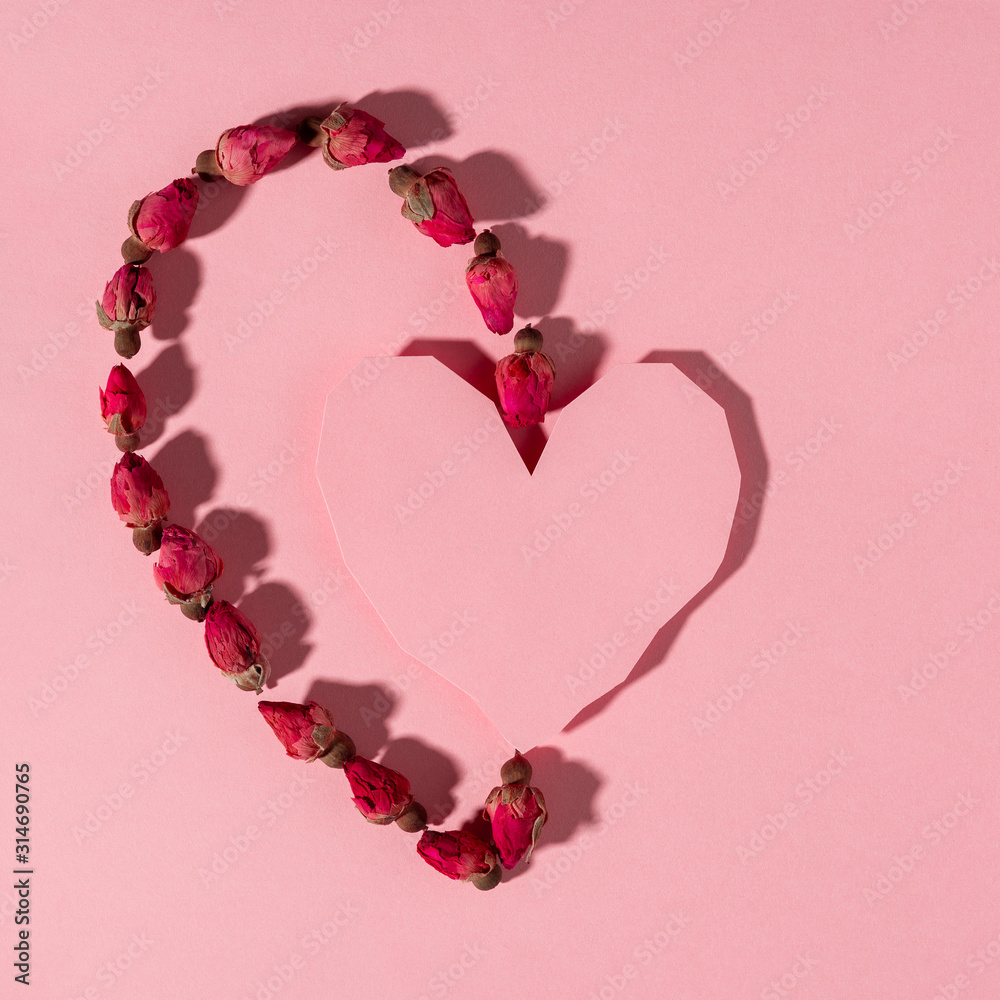 Conceptual background of Valentine's day, pink heart made of paper, dry rose flowers arranged on the pink background