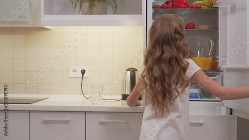 Cute little girl opening refregirator to take orange juice photo