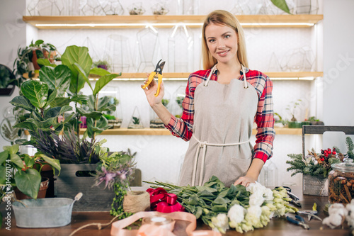 flowers composing and decoration by young lady with blonde hair, wearing red checkered shirt, isolated in light room full of green plants. botany, flowers concept