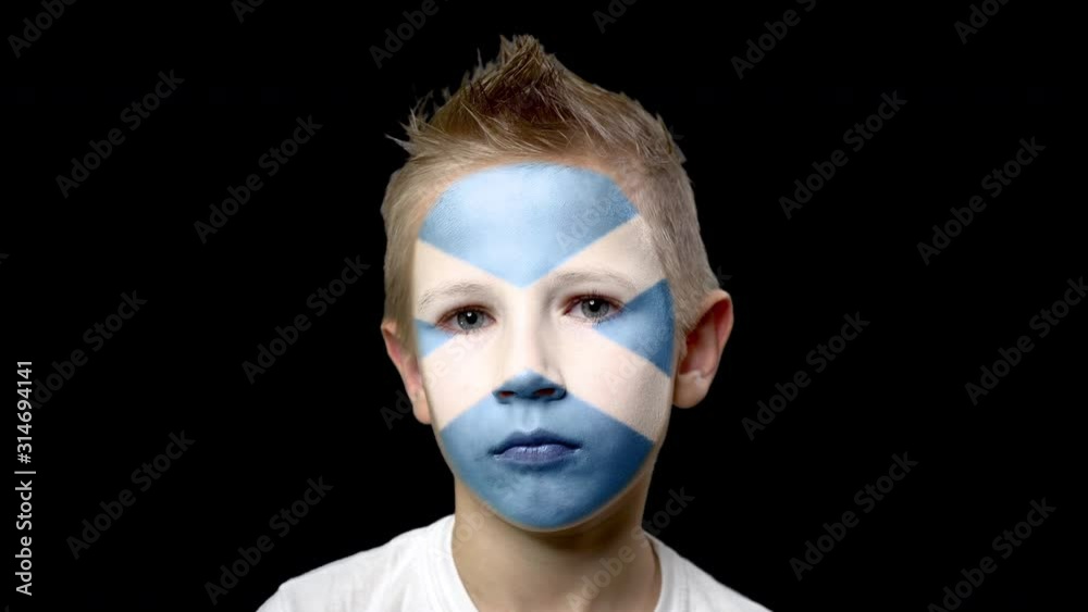 Sad fan of the football team of Scotland. A child with a face painted in national colors. Unhappy boy with sad eyes. Fiasco of your favorite team. Disappointment. Sadness. Experience. Failure. Sad fan of the football team of Scotland. A child with a face painted in national colors. Unhappy boy with sad eyes. Fiasco of your favorite team. Disappointment. Sadness. Experience. Failure.