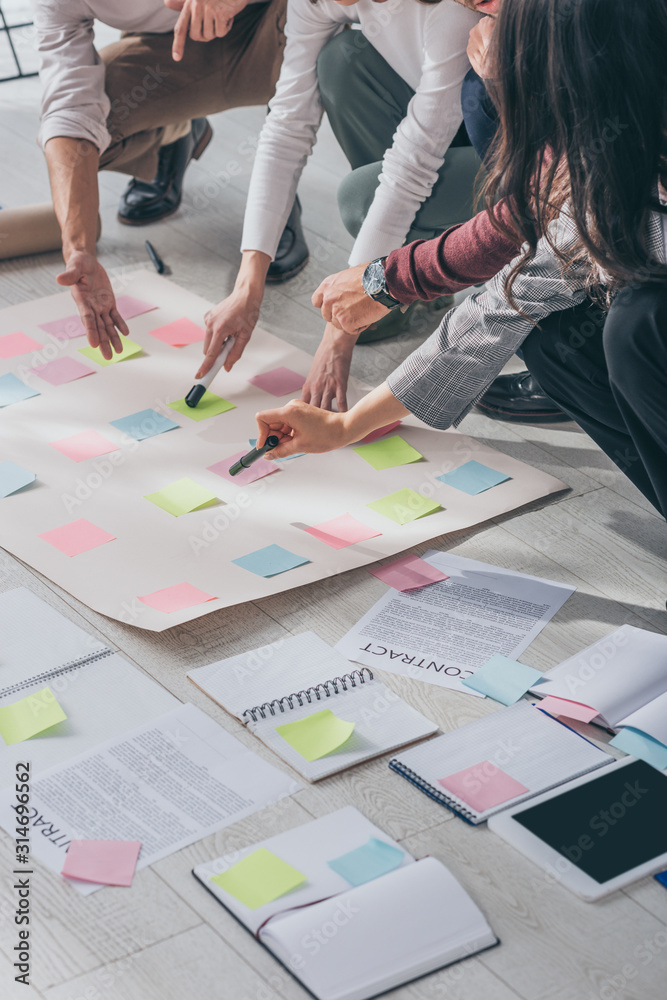 cropped view of scrum masters pointing with fingers at floor with sticky notes near documents cropped view of scrum masters pointing with fingers at floor with sticky notes near documents