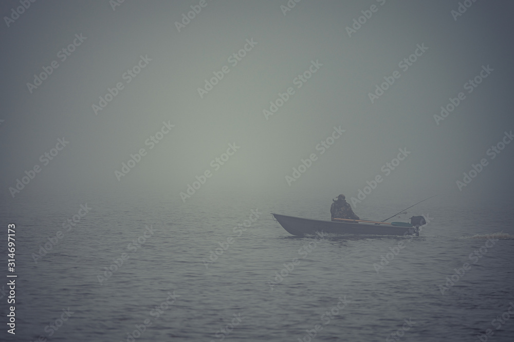 lonely fisherman on a boat, heavy fog on the lake