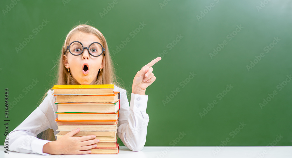 Surprised girl with books points on empty chalk board. Empty space for text Surprised girl with books points on empty chalk board. Empty space for text