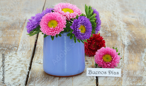 Obraz na płótnie Buenos dias (good morning in Spanish) card with colorful daisies in blue vase on rustic wooden surface w salonie