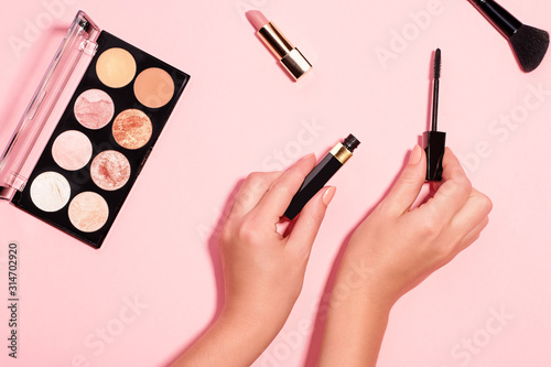 Woman hands holding open black mascara on pastel pink background, top view. Minimal beauty background with makeup products, flat lay, copy space. Eye and face make up concept