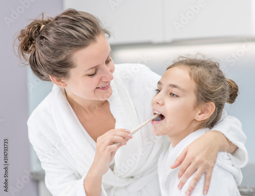 Happy family at home. Young mother teaches her cute daughter how to brush teeth with toothbrush