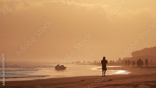 hombre con el sol de fondo al atardecerbre caminando en la playa con el sol de fondo