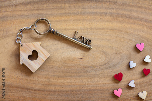 House key in heart shape with home keyring on old wood background decorated with mini heart