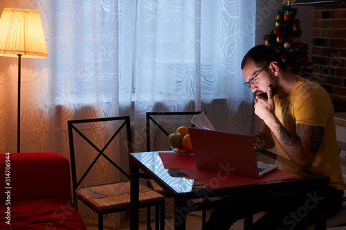 young caucasian businessman work on laptop at home, hardworking male in casual wear sit in kitchen using modern laptop, with docuents on table photo