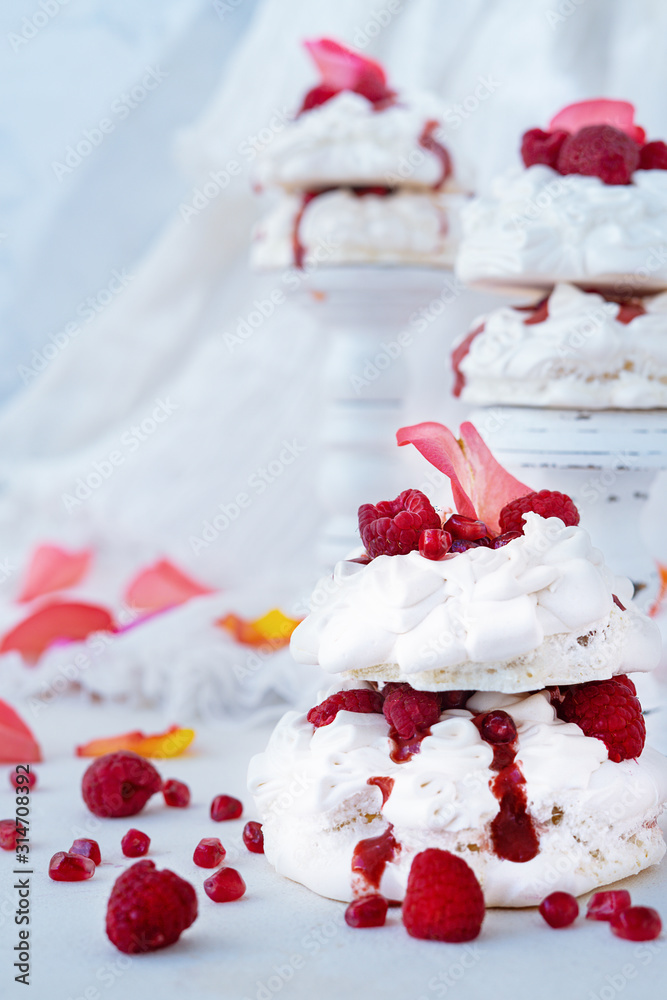 Pavlova cakes with raspberries and rose petals and pomegranate seeds on white background. Valentine or wedding concept Pavlova cakes with raspberries and rose petals and pomegranate seeds on white background. Valentine or wedding concept
