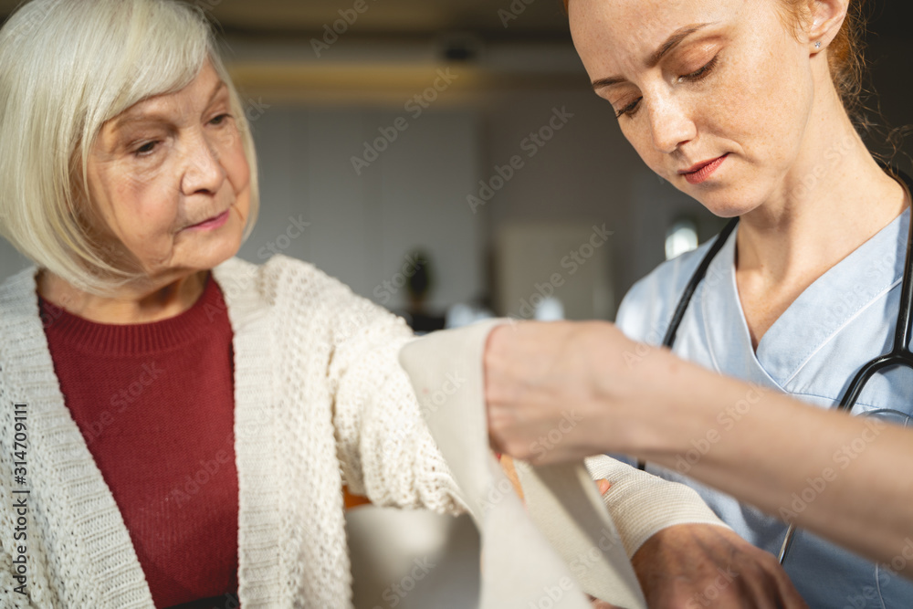 Obraz premium Attentive mature female person putting bandage on arm