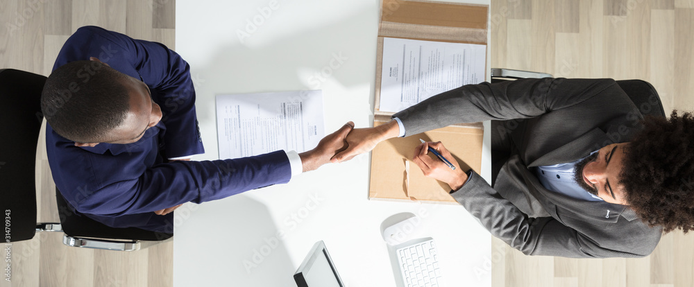 Young Businessman Shaking Hand With Candidate Over White Desk - obrazy, fototapety, plakaty 