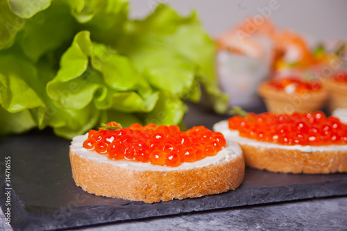 Fresh red caviar on bread on the black plate. Sandwiches with red caviar. Delicatessen. Gourmet food.