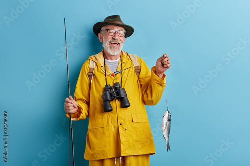 bearded positive man holding cought fish, being happy to catch it. close up photo.isolated blue background, studio shot . lifestyle, people