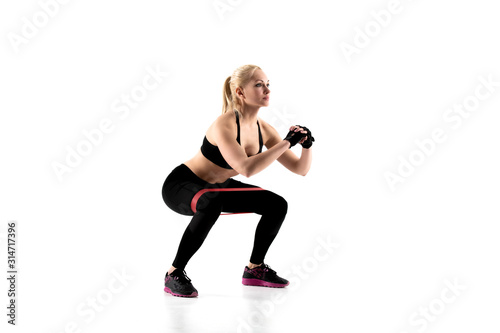 Fototapeta Naklejka Na Ścianę i Meble -  The girl performs squats with an expander during training.