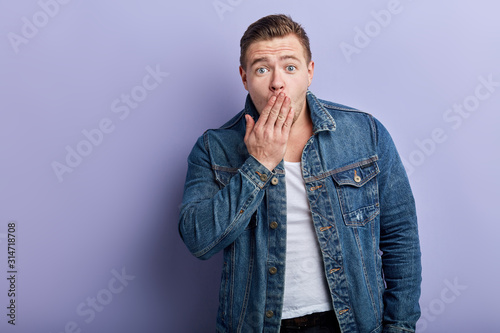 Portrait of a surprised anxious man covering his mouth with his hands, feels stunned and scared. isolated blue background, reaction, facial expression. oh, my God, man has heard shocking news