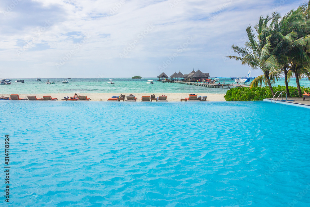 Blue swimming pool water and palm trees near the sea. Summer vacations in tropical resort.