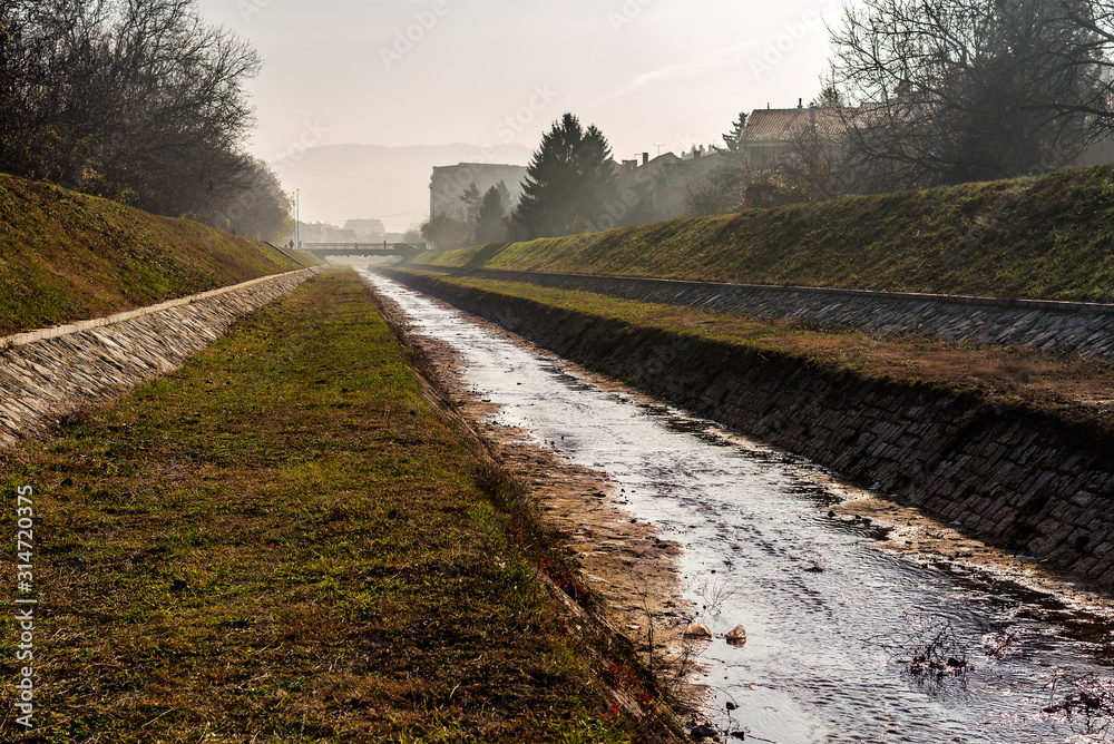 Fototapeta premium Gabrovacka River - Gabrovacka reka channel on the outskirts of the City of Nis in Serbia, with low water level on the autumn foggy day.