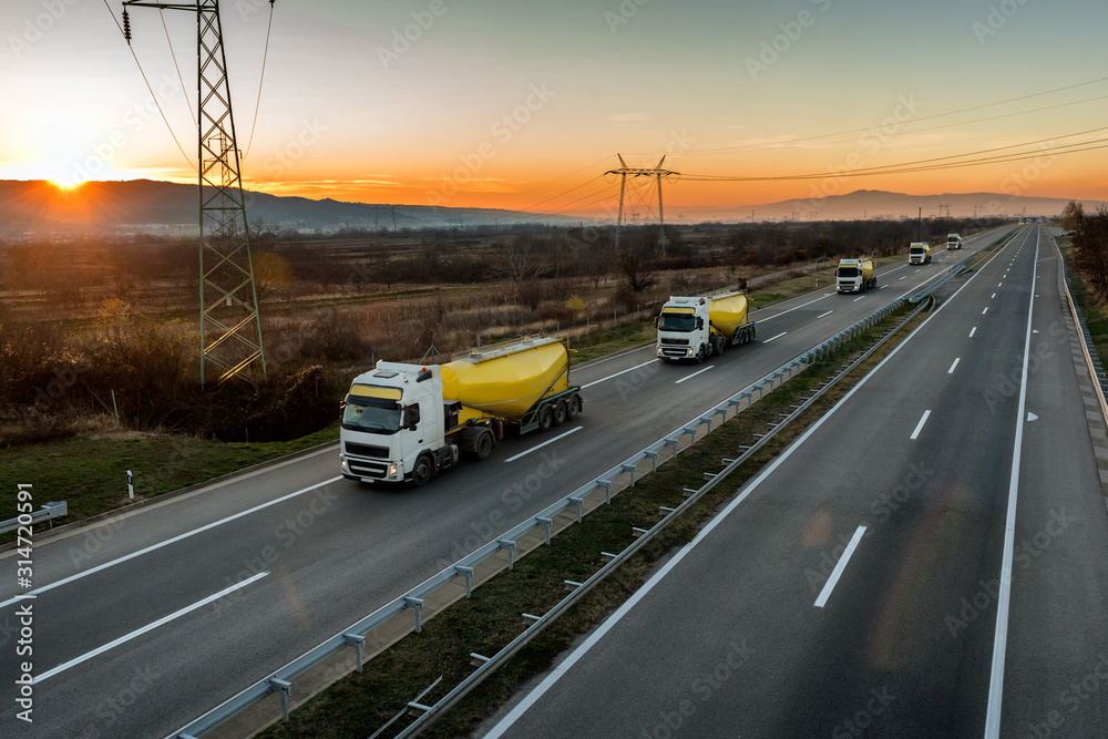 Convoy or Caravan of white and yellow Tank trucks on a Highway traffic through the rural landscape at beautiful sunset