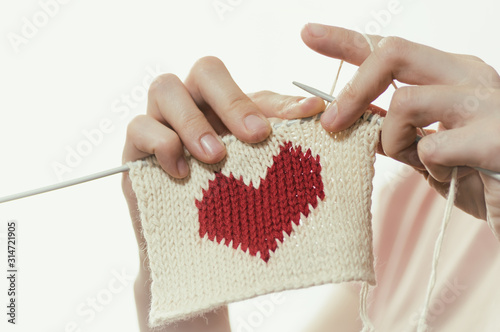 Concept of love and concern. Woman knitting the red heart for her loved one. Valentines postcard.