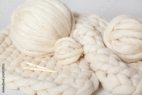 a ball of thick yarn and wooden needles lie on a blanket of Merino wool