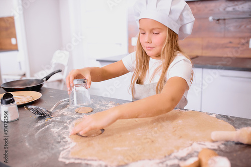 nice and beautiful little girl baking, forming circle forms from dough with the use of cup.