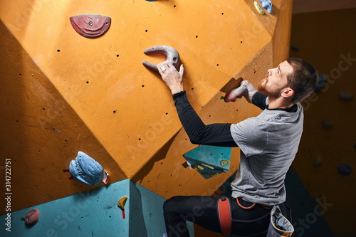 Side view of professional rock-climber without forearm training indoors at colorful climbing wall in bouldering gym, prepairing to oncoming ascend, working out most complicated problems.