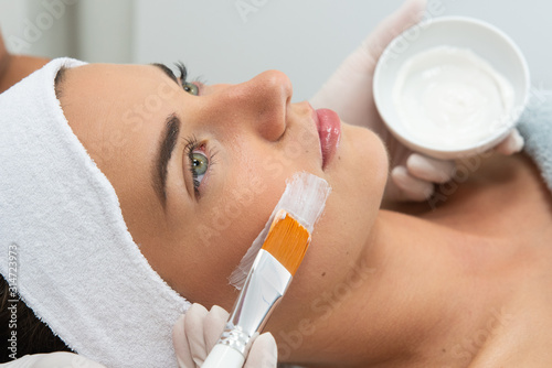 Dermatolog wykonuje zabieg leczniczy na twarzy kobiety. Maska w salonie kosmetycznym. Kosmetyczka trzyma w dłoni pędzel i nakłada kosmetyk na twarz kobiety.