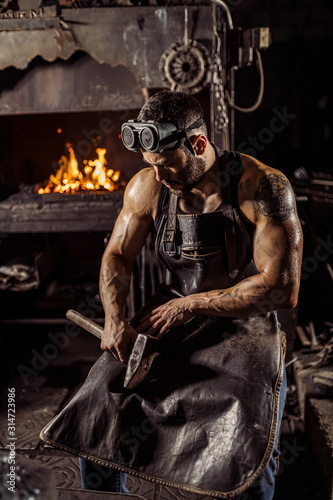 portrait of strong muscular handsome forger in leather uniform isolated in workshop, furnace fire in the background