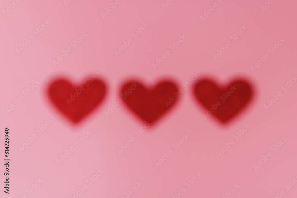 Three red heart shape figures out of focus on the background