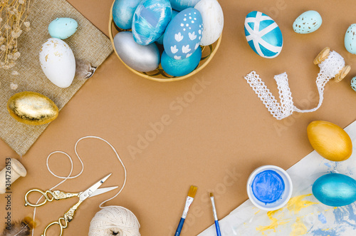 Frame Easter eggs painting workspace. Paints, paint brushes, ribbons and twine. Copy space for your text on a craft paper background. Top view photo