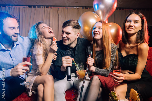 young women and men clubbers spend time in karaoke bar, have fun singing in microphone. leisure, celebration, party concept